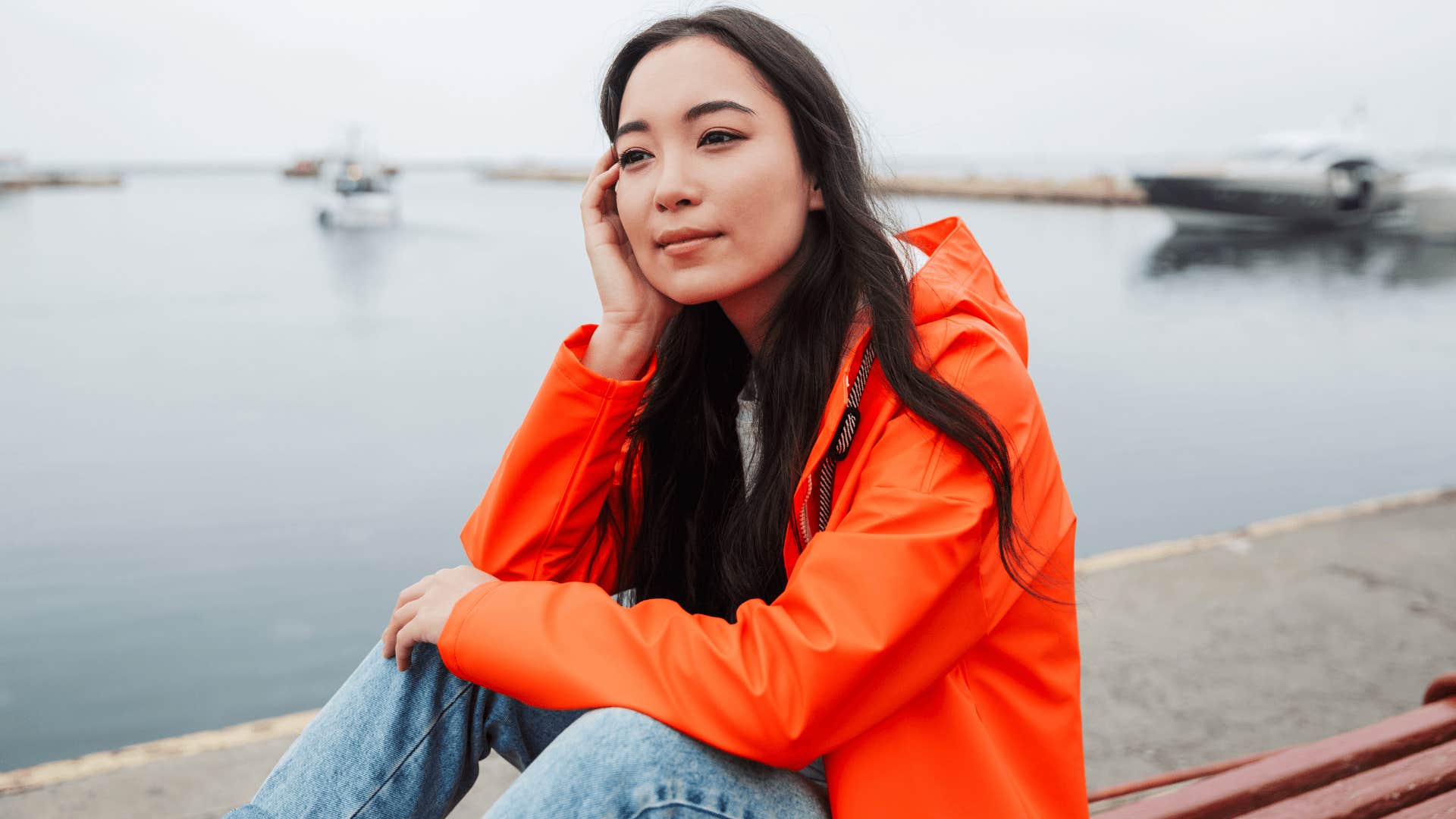 woman in orange by the water releasing emotions that no longer serve her