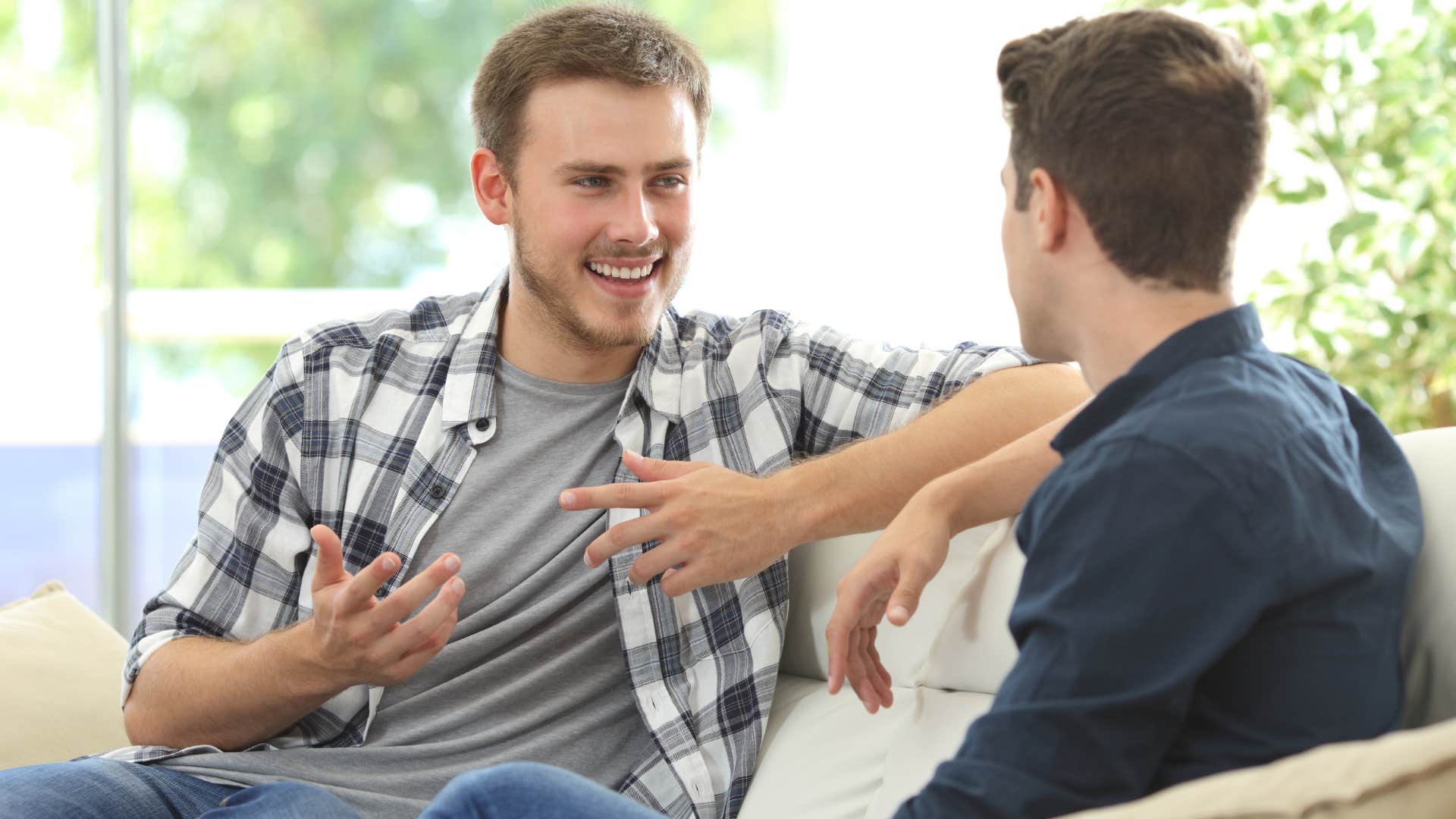 man in checkered shirt describing something that made him happy recently while sitting on the couch with guy in dark shirt