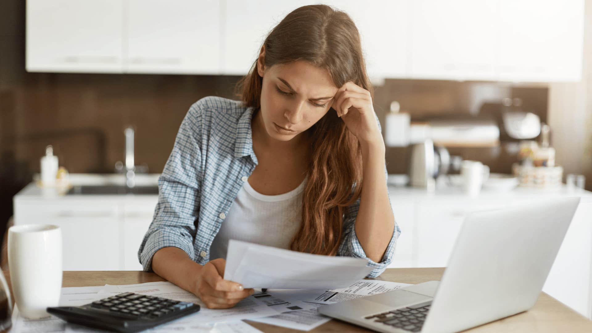 woman feeling as if she's not bringing in enough money looking at paper in frustration with her head in hand