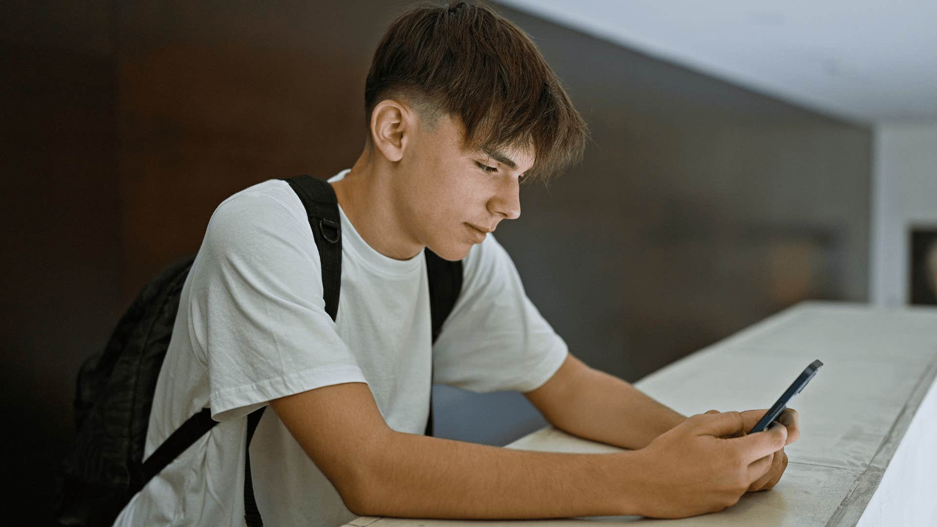 Young man senses subtle energy shifts while texting on his phone with a backpack on