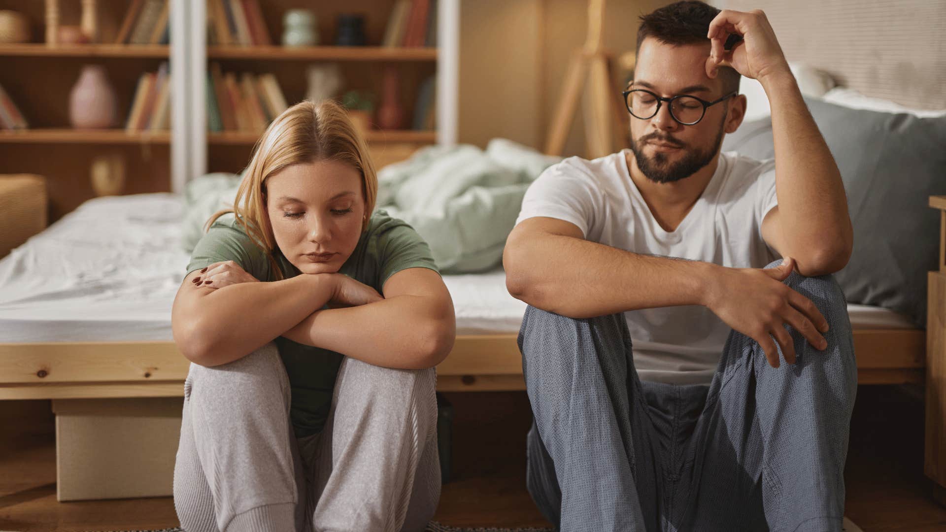 couple who has different core values sitting on the floor near their bed looking upset