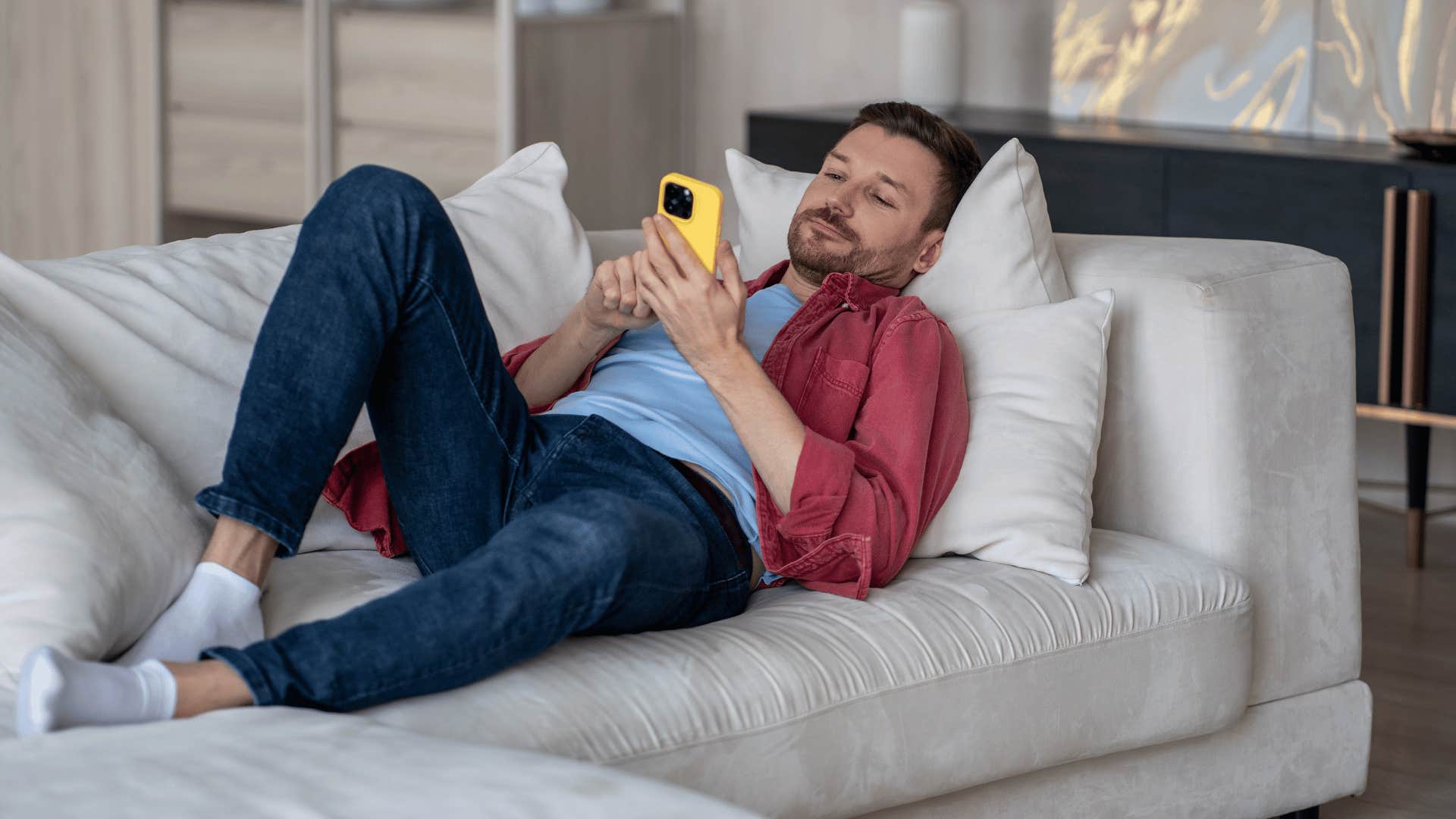 unmotivated husband lays on the couch looking at his phone