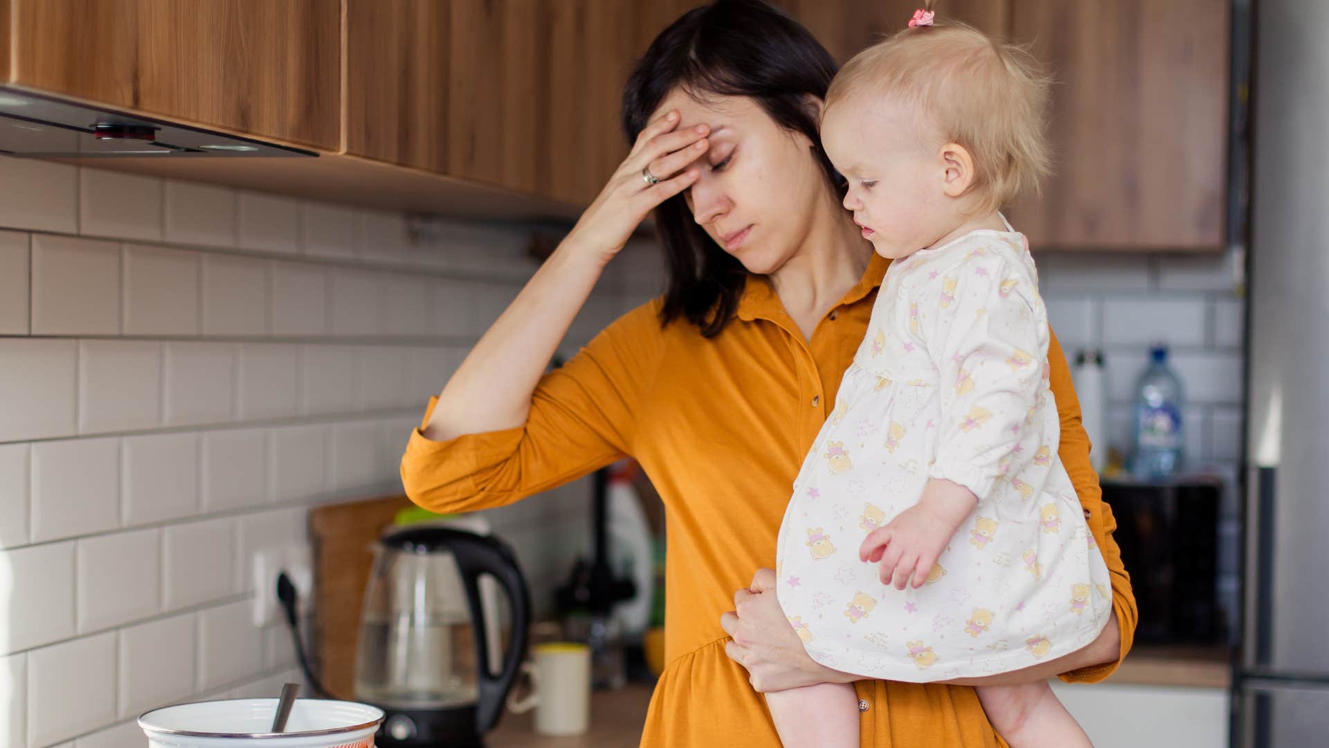 stressed woman holding baby trying to wash dishes