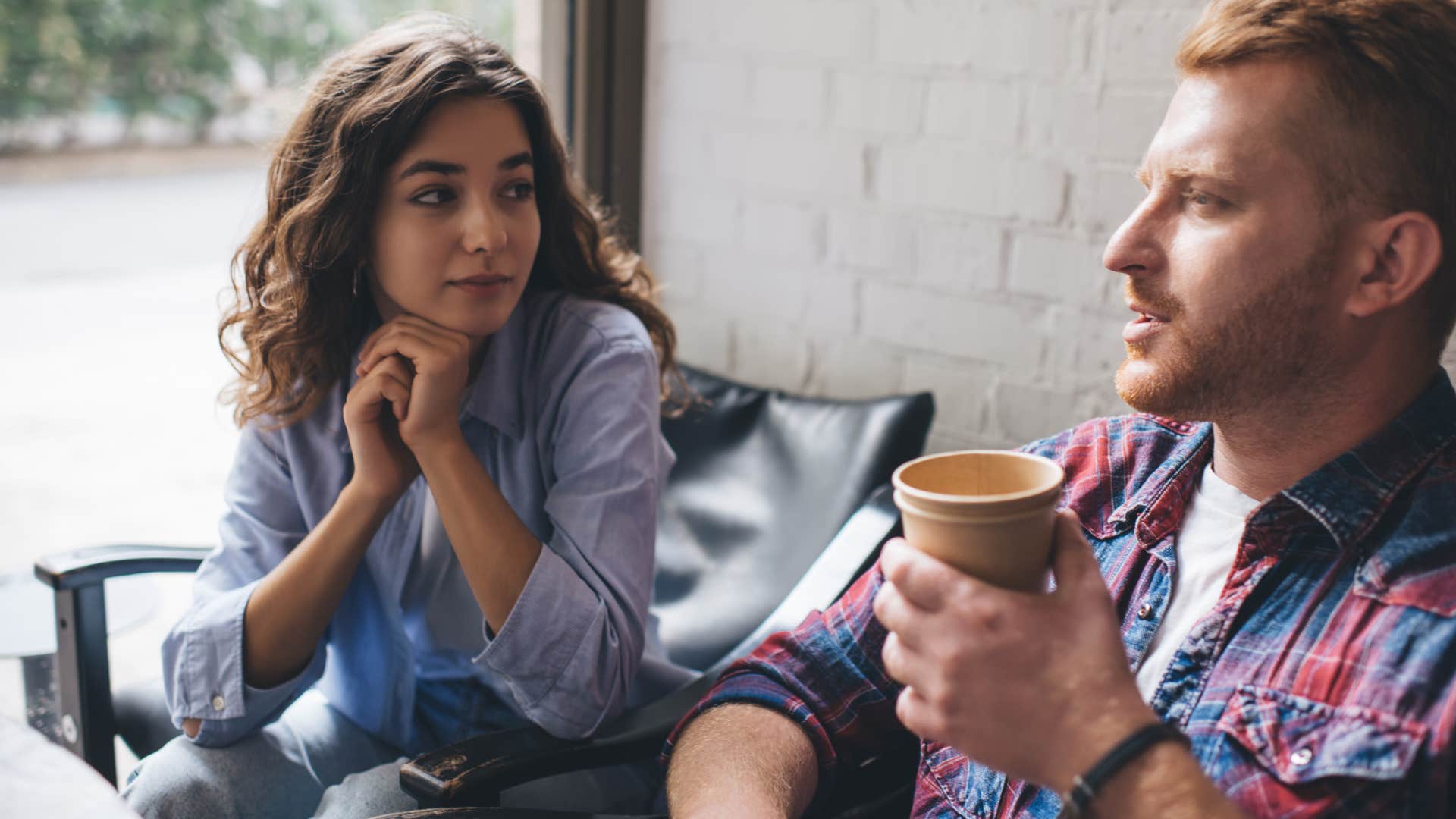 woman giving man a side eye and thinking that's one way to look at it as he talks with a cup of coffee in his hand