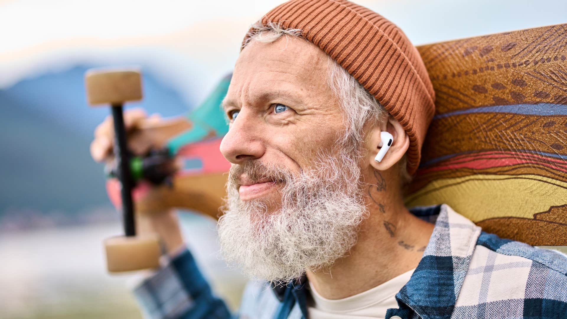 Baby boomer with great hobbies smiling outside with a skateboard.