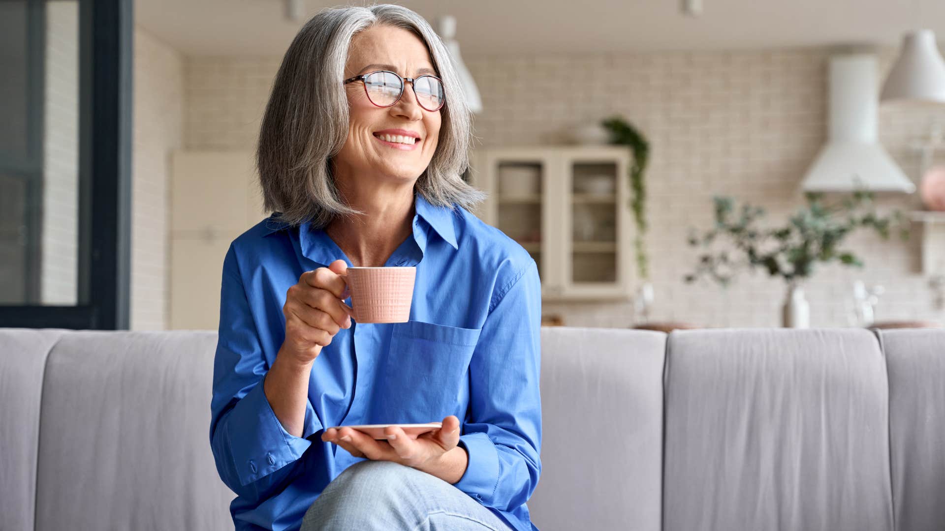 Woman who knows how to unplug smiling on her couch with a cup of coffee.