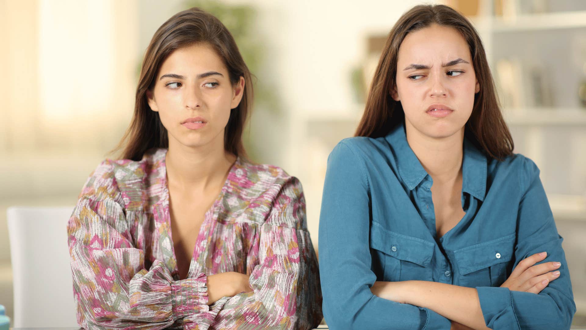 two women avoiding admitting they're wrong as they cross arms and glare at one another on the couch