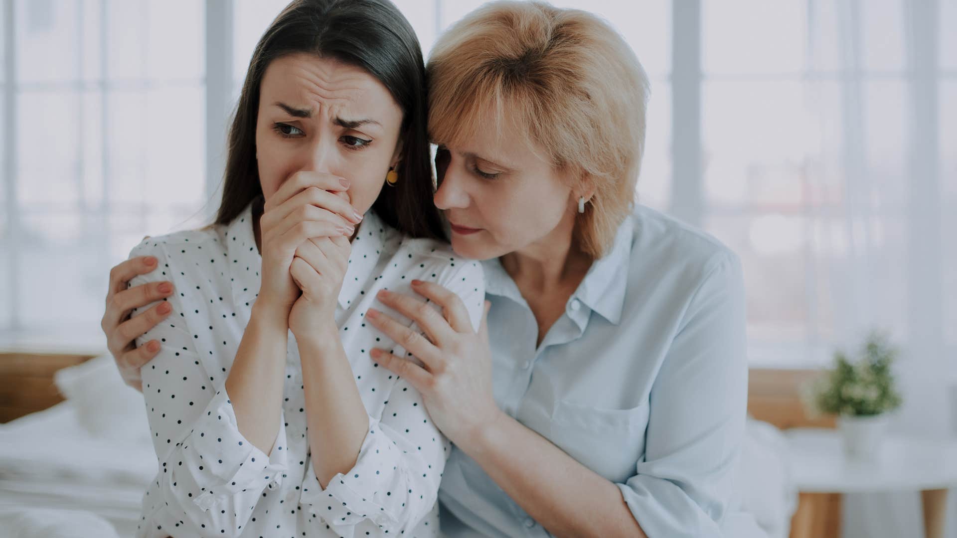 woman comforting her upset adult daughter on a couch