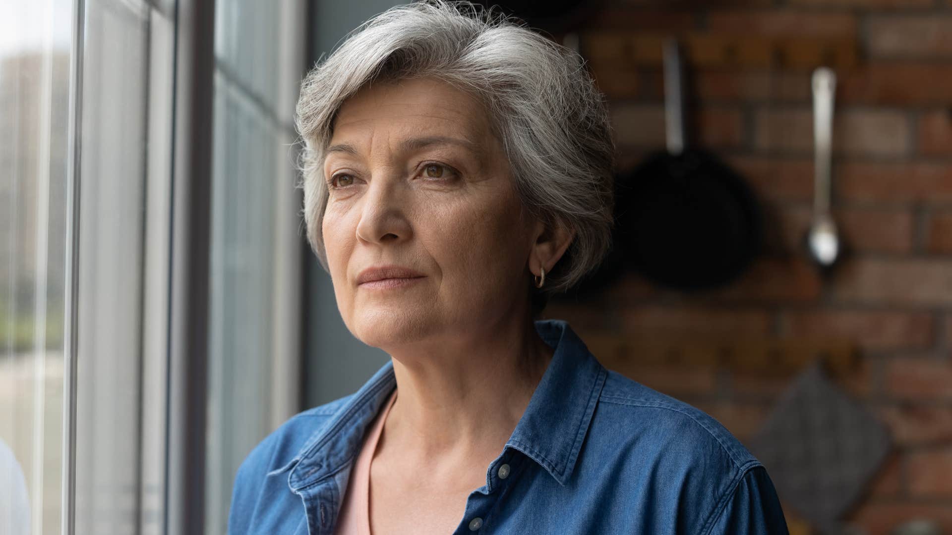 upset older woman looking out window thinking about retirement