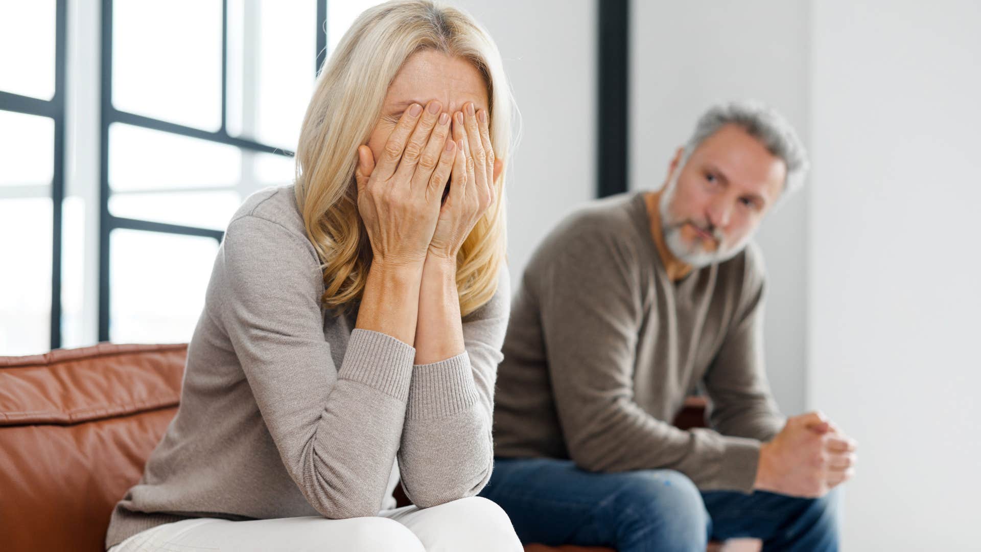 upset woman covering her face as man looks at her