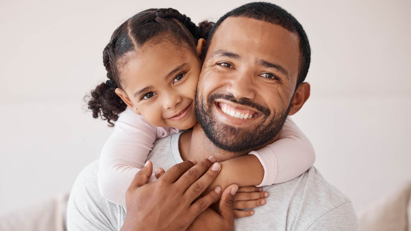 smiling dad holding young daughter raising her to be confident