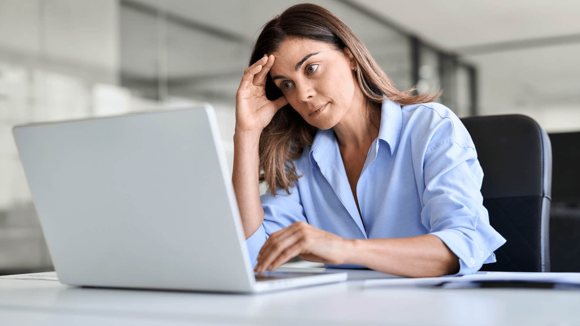woman frustrated and working hard on assignment as she stares at laptop with head in hand