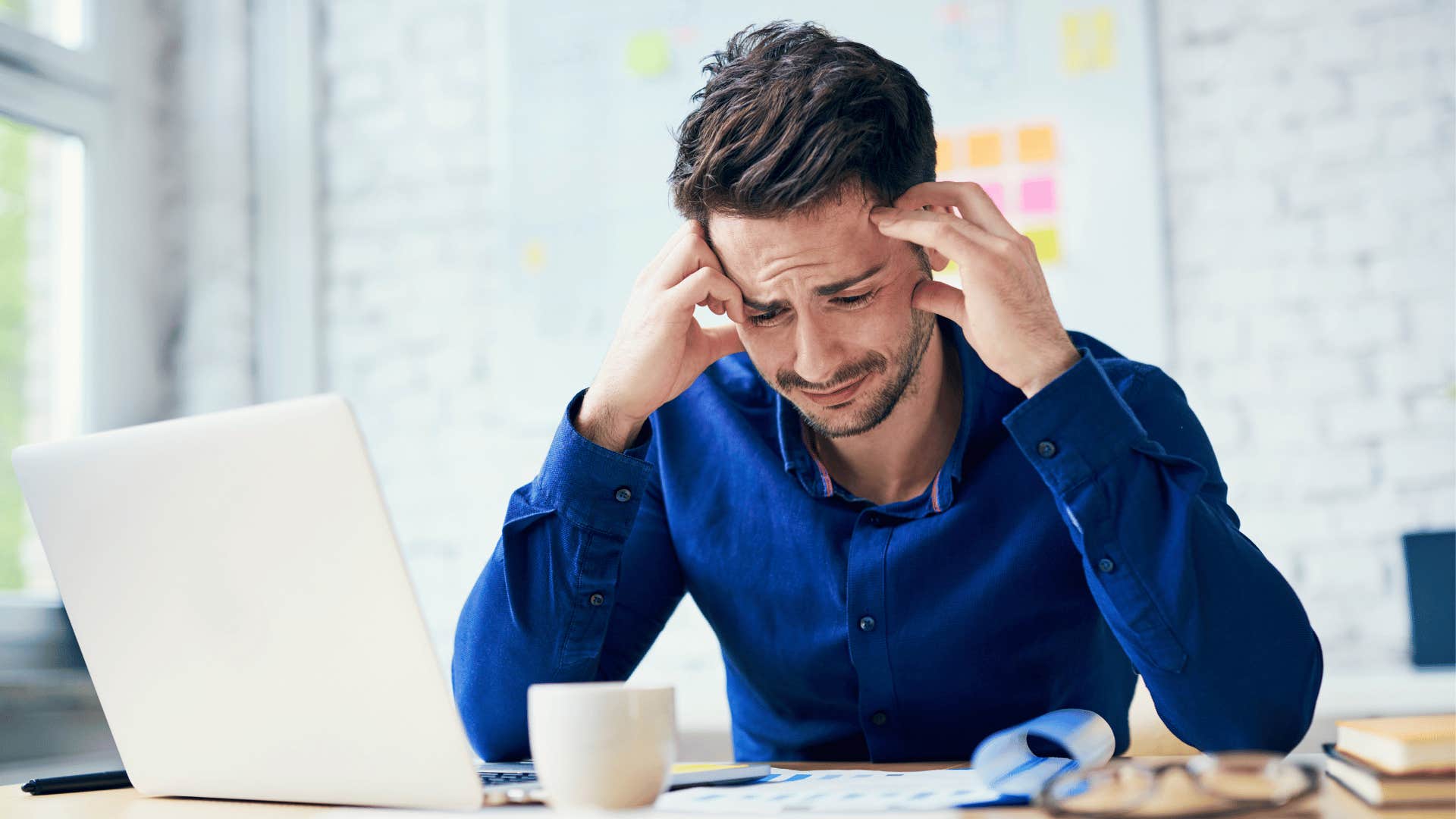 A young gen z worker struggles with his mental health at his desk.