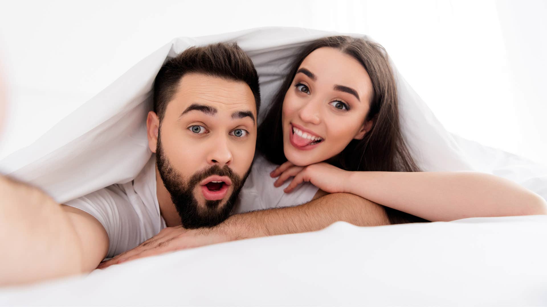 couple under covers in bedroom smiling