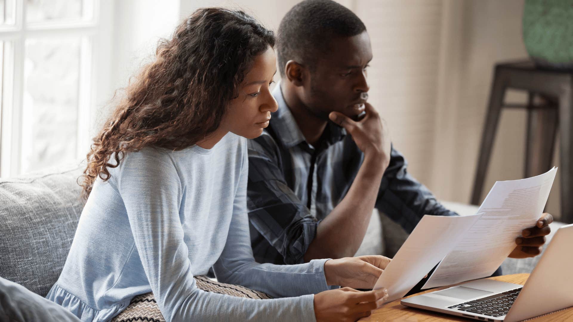 Stressed couple doing bills on their couch aren't able to live a financially comfortable life