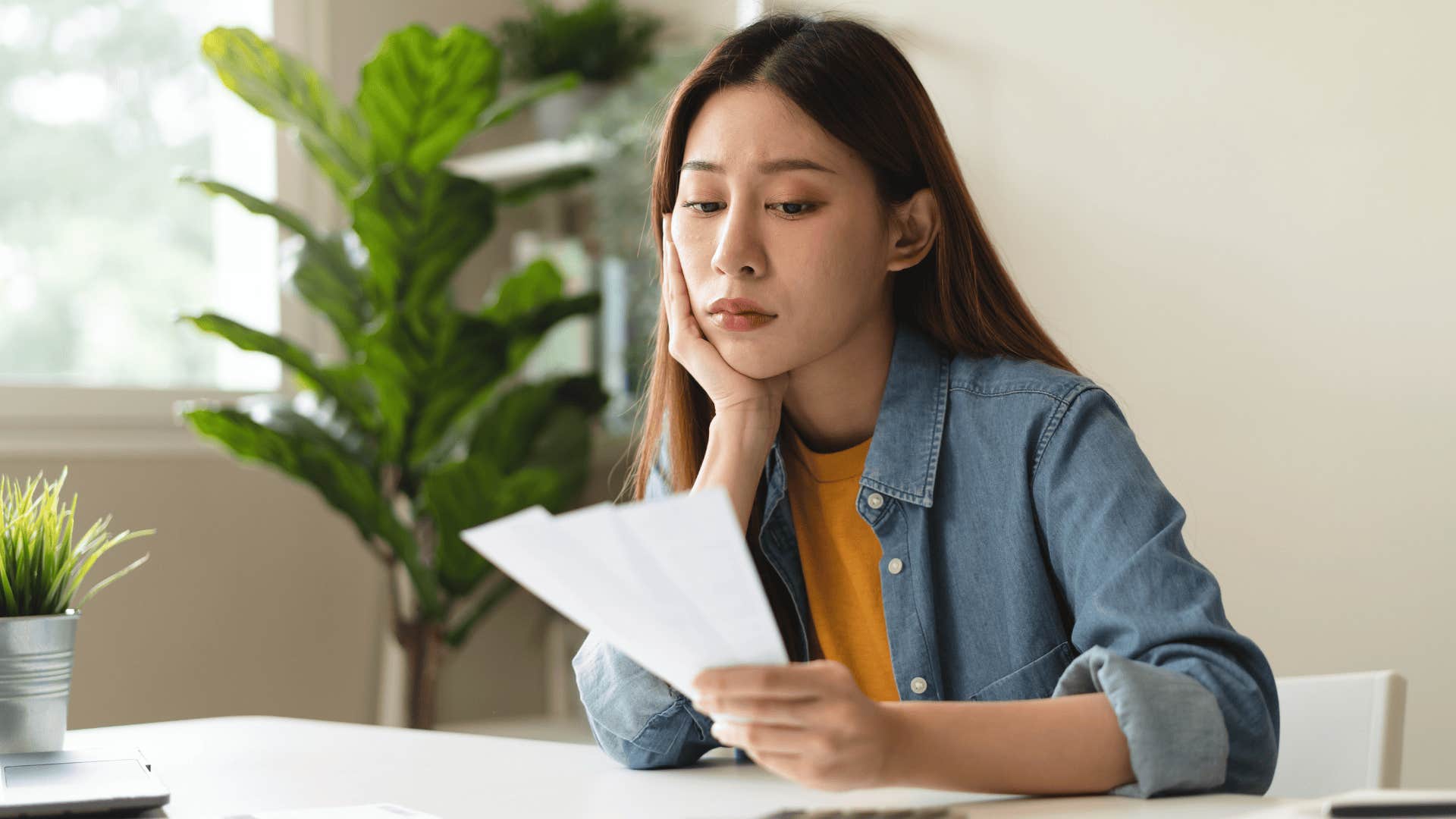 Upset woman with no disposable income reading her bills at a kitchen table