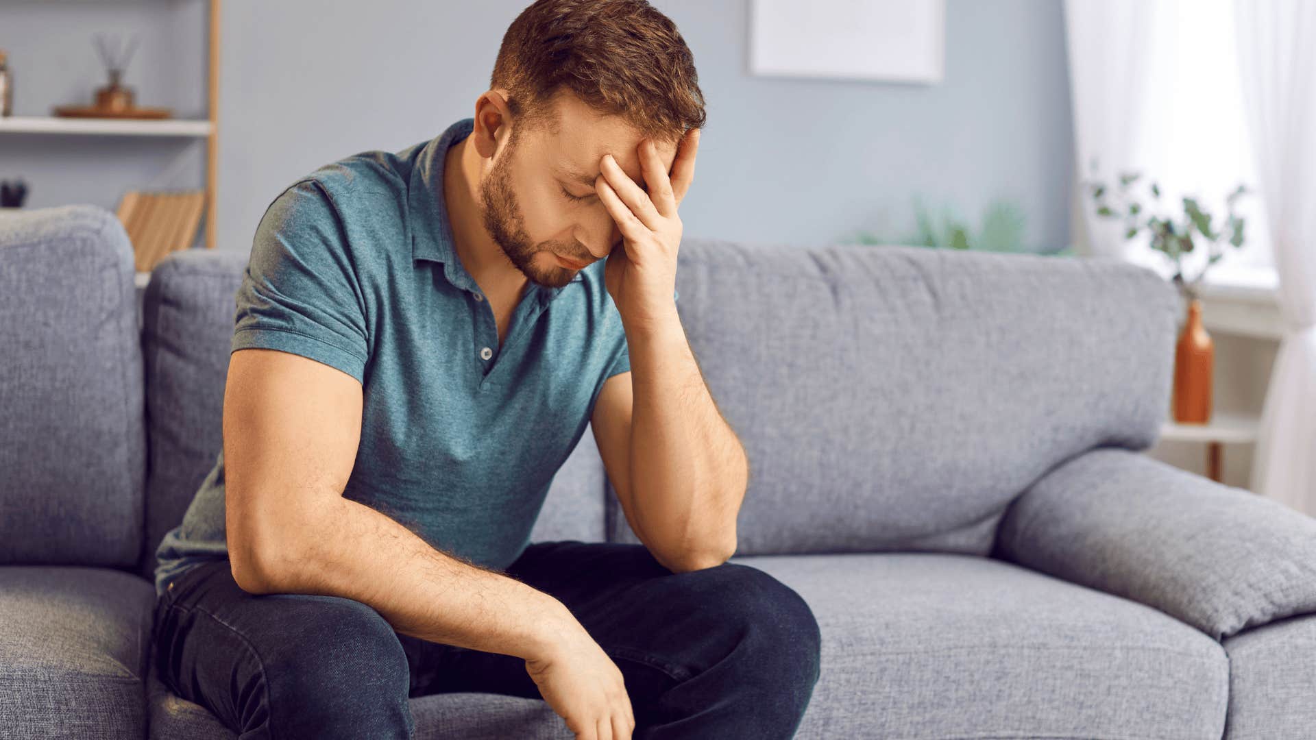 Upset man worried about buying a home holds his face in his hands on couch