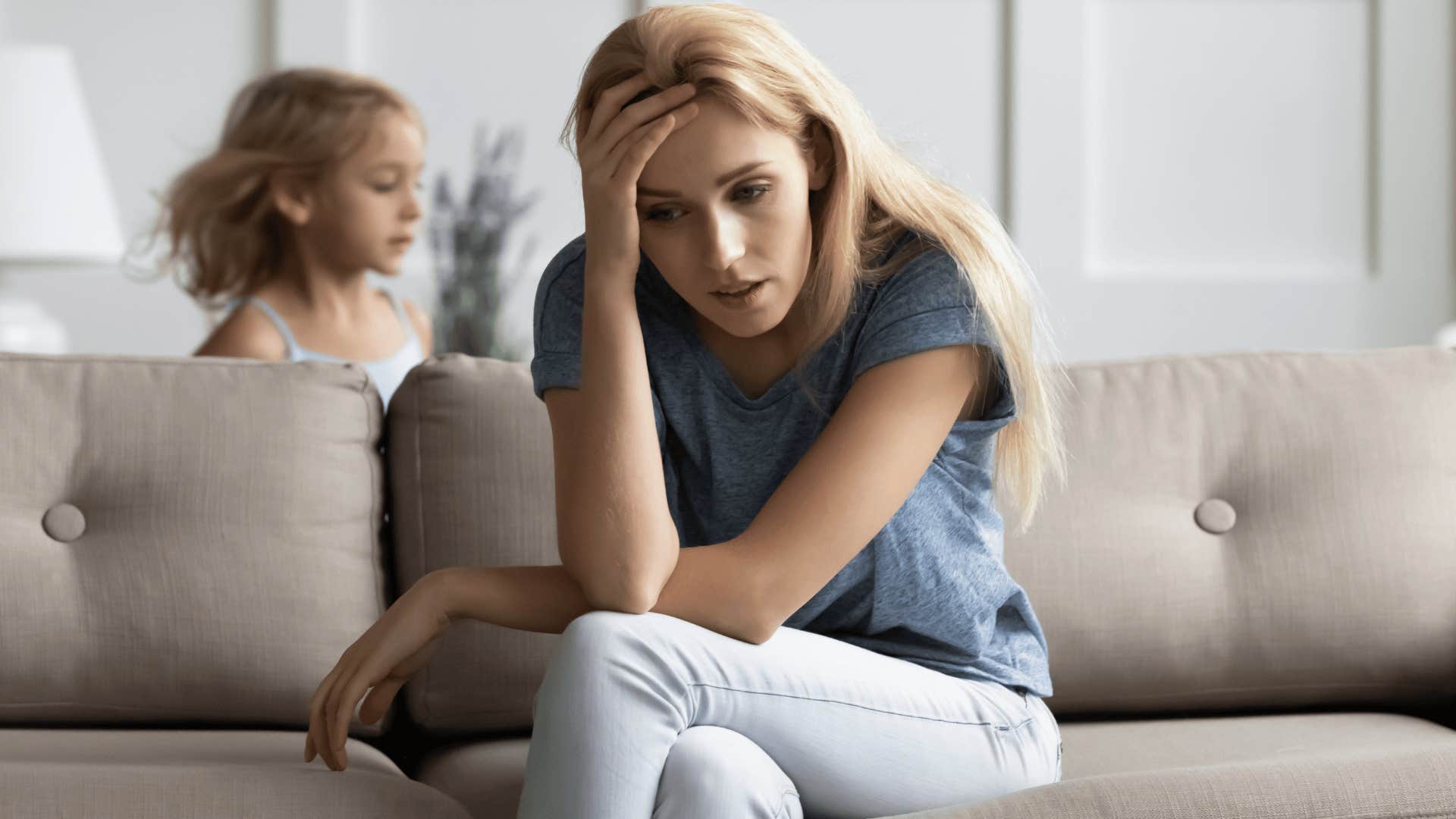 Stressed mother who can't afford childcare sitting on a couch while her kids run around her