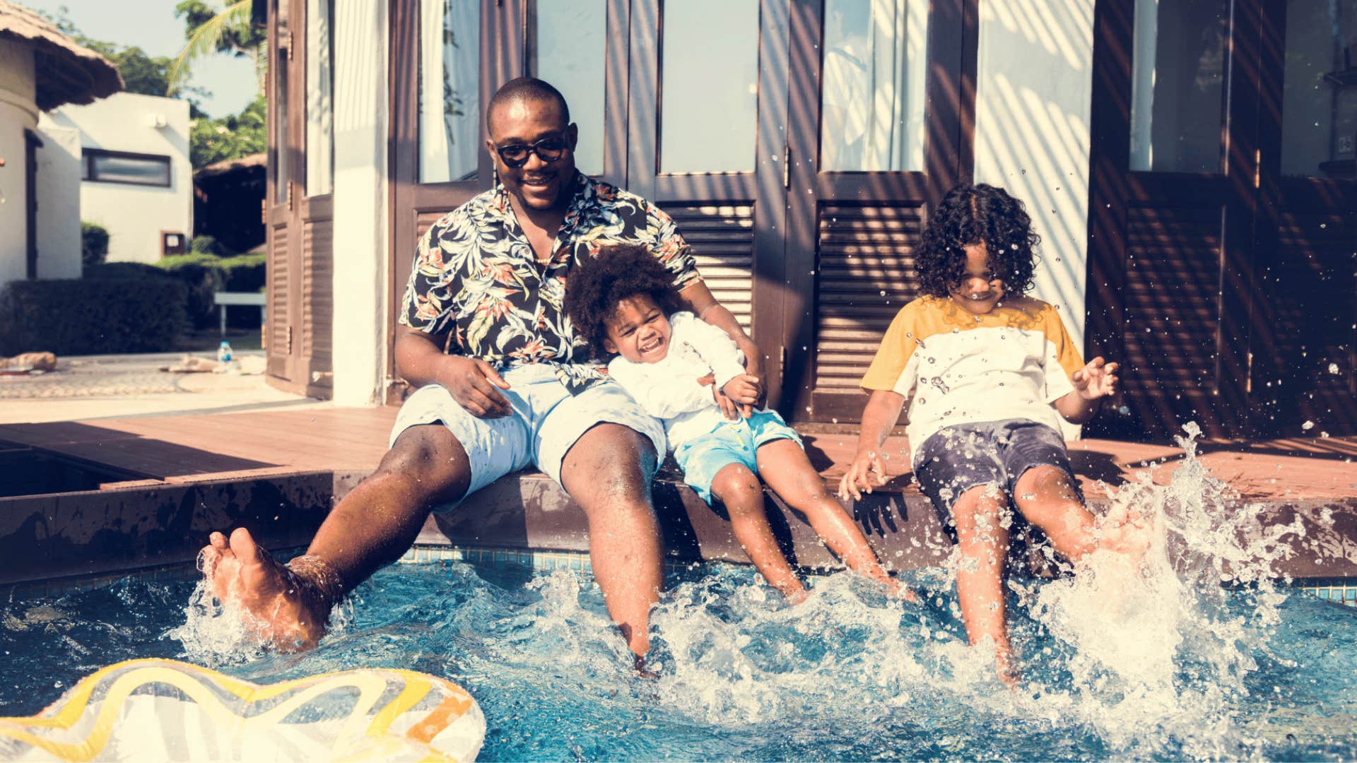 A father plays in the backyard pool with his two children.