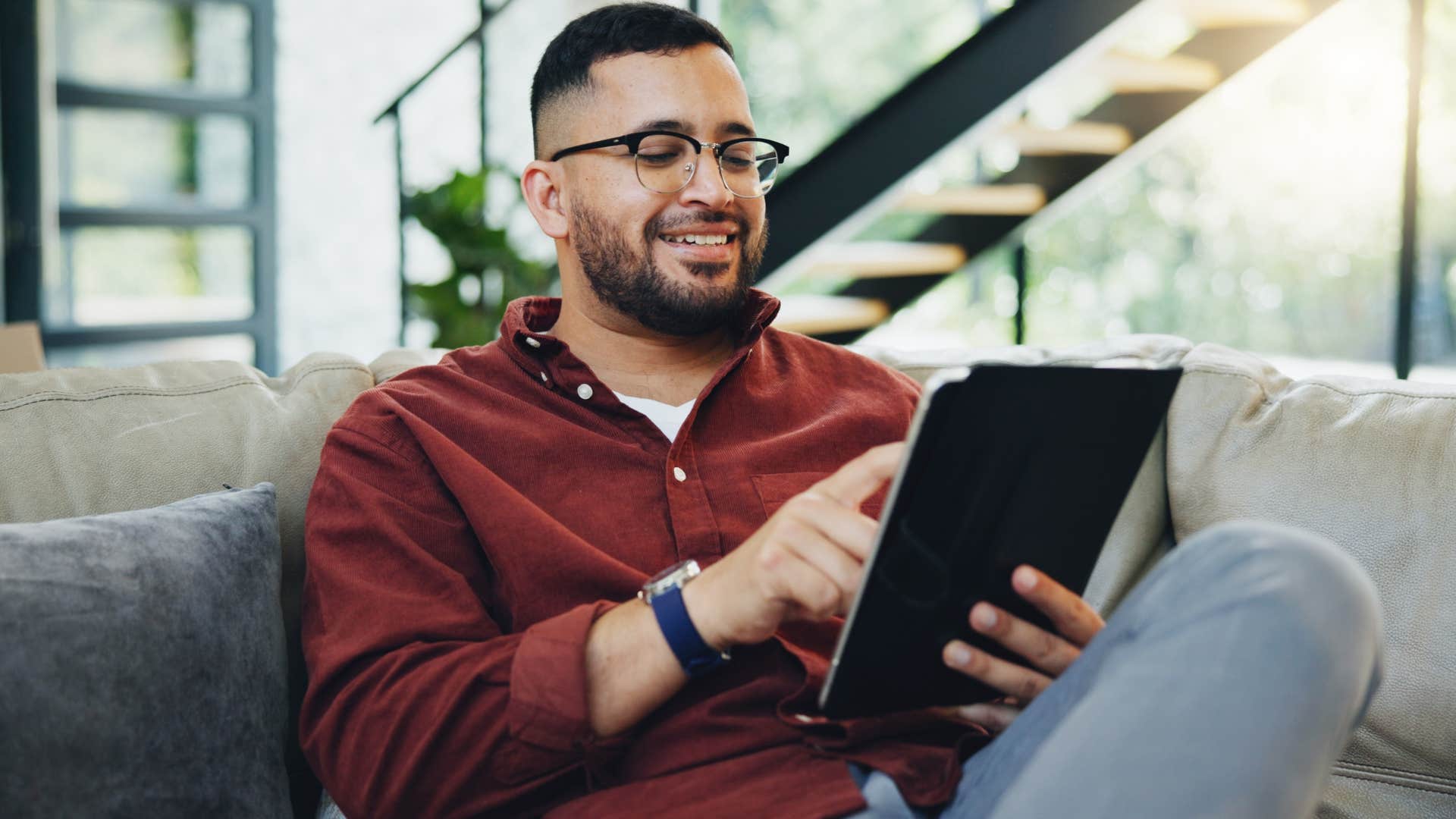 Man who doesn't entertain drama smiling and looking at a tablet at home.