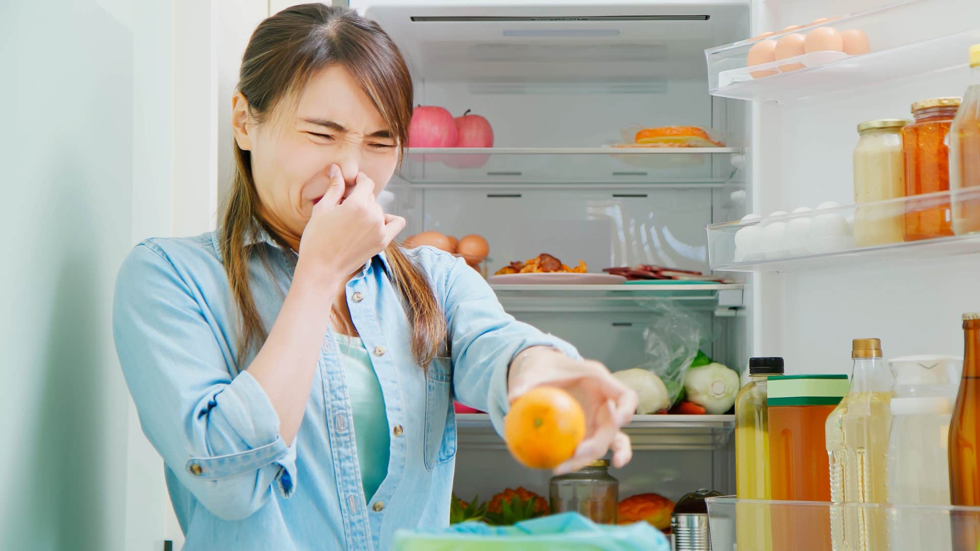 woman holding her nose throwing away old food in fridge