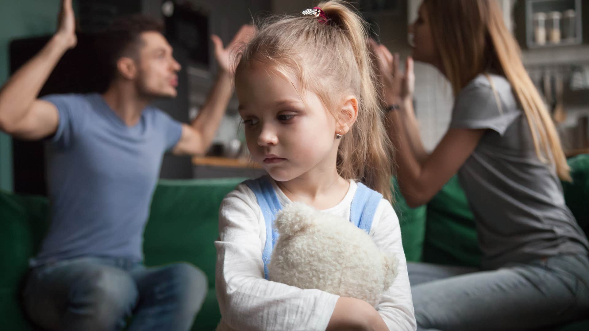 upset young girl sitting in front of arguing parents