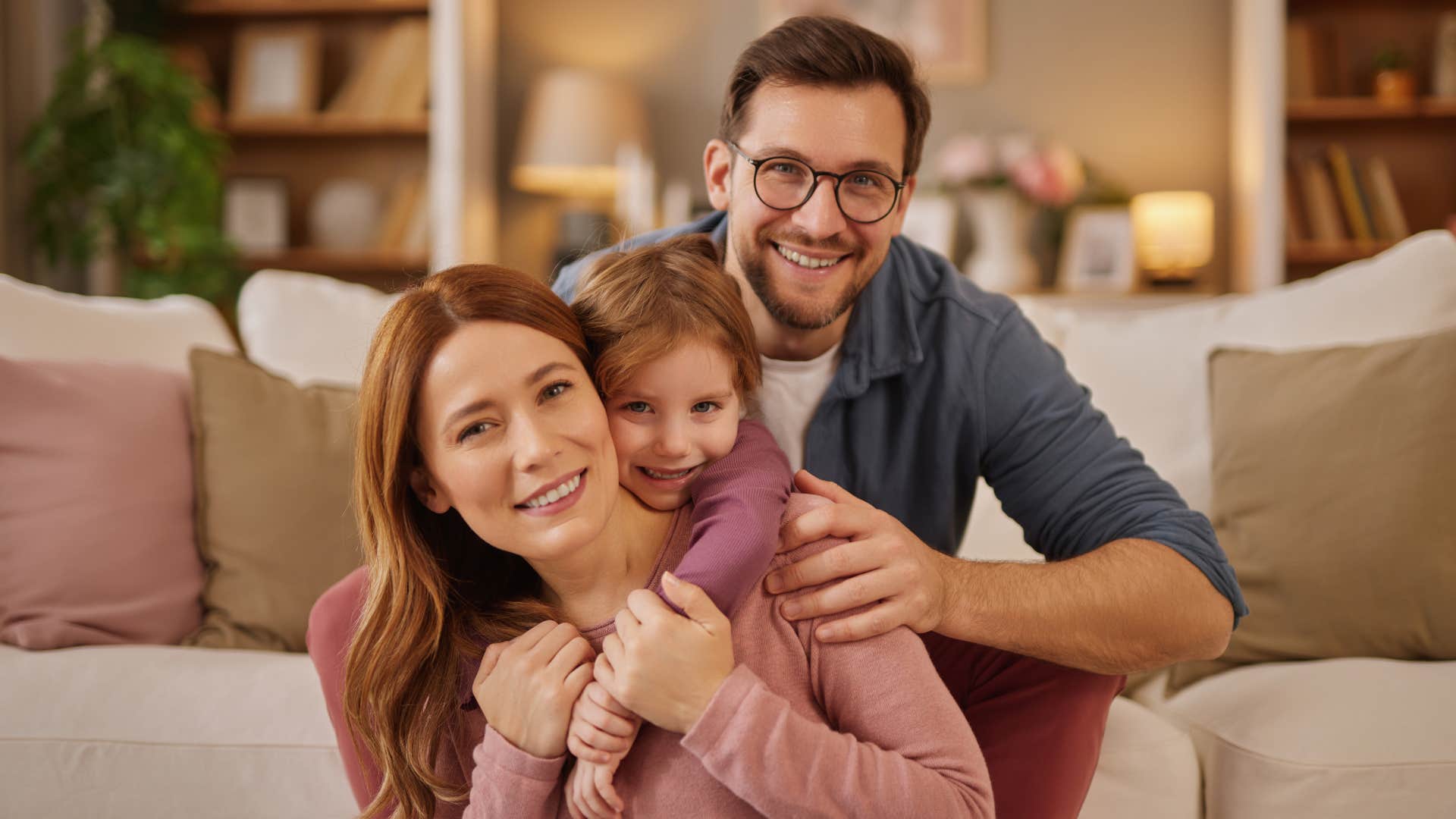 A husband and father plays in the living room with his wife and child.