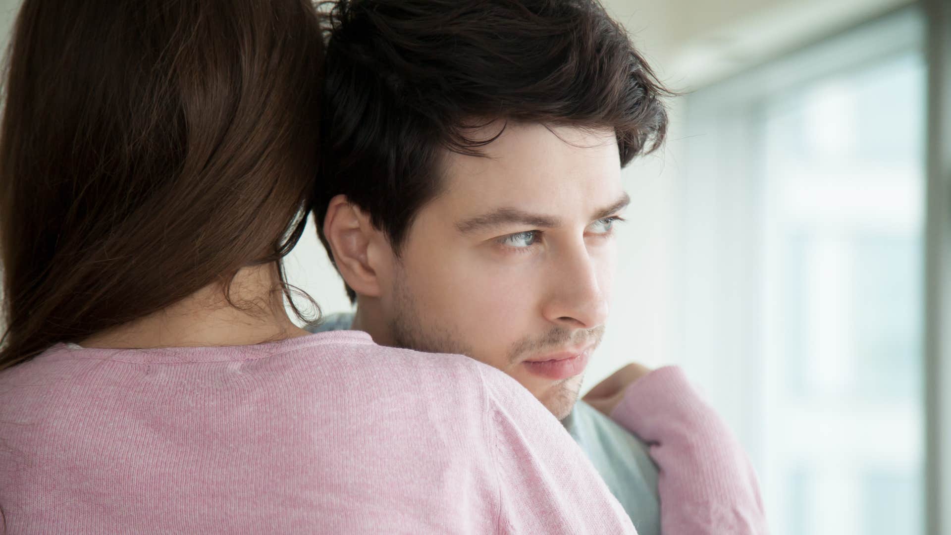 Man thinking "Are you mad at me?" while hugging his wife.