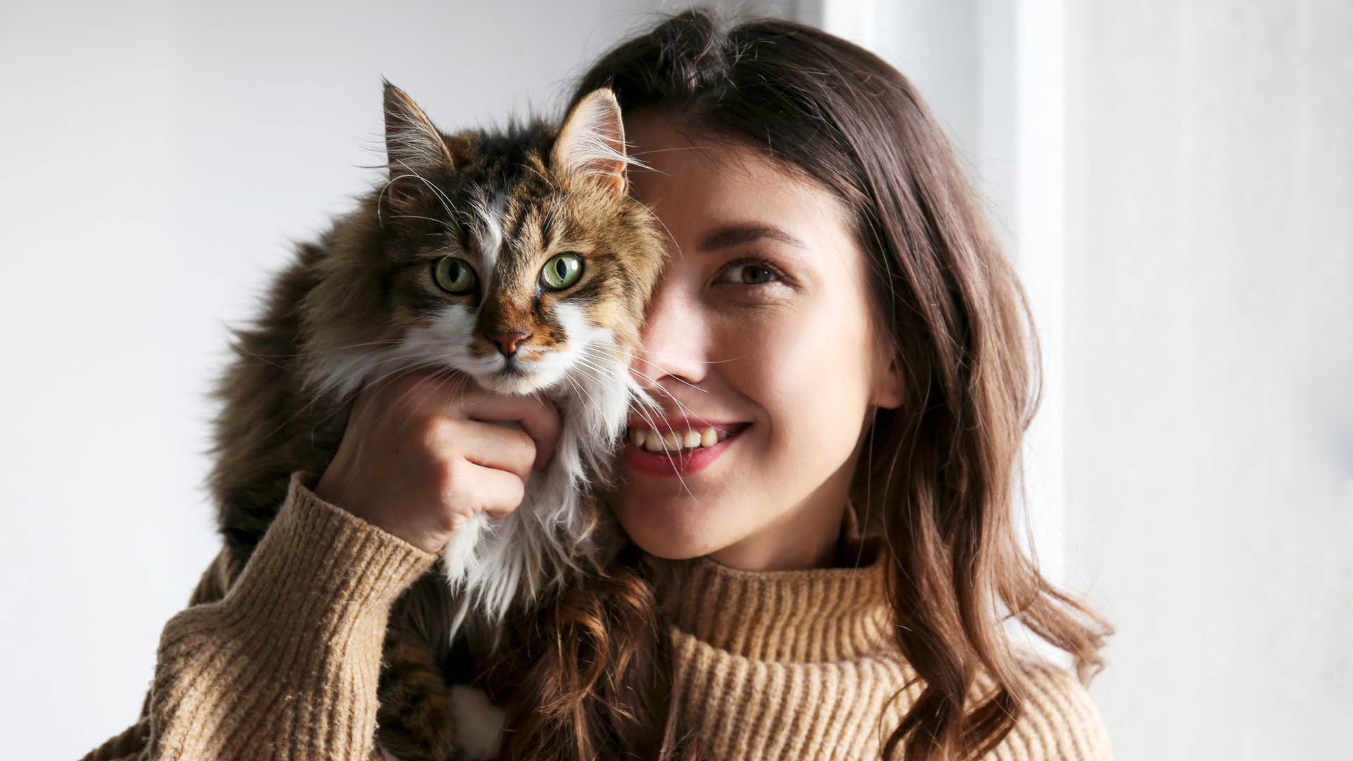 woman holding cute cat up to her face smiling