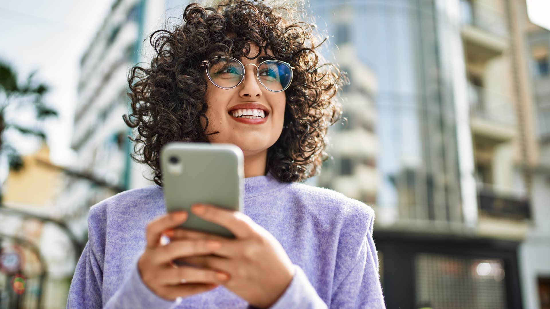 Reliable woman smiling outside on her phone.