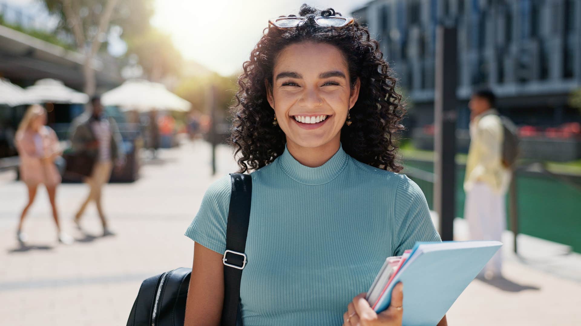 woman in blue shirt holding notebook and smiling at the camera as she refuses to put her dreams on the backburner for anyone