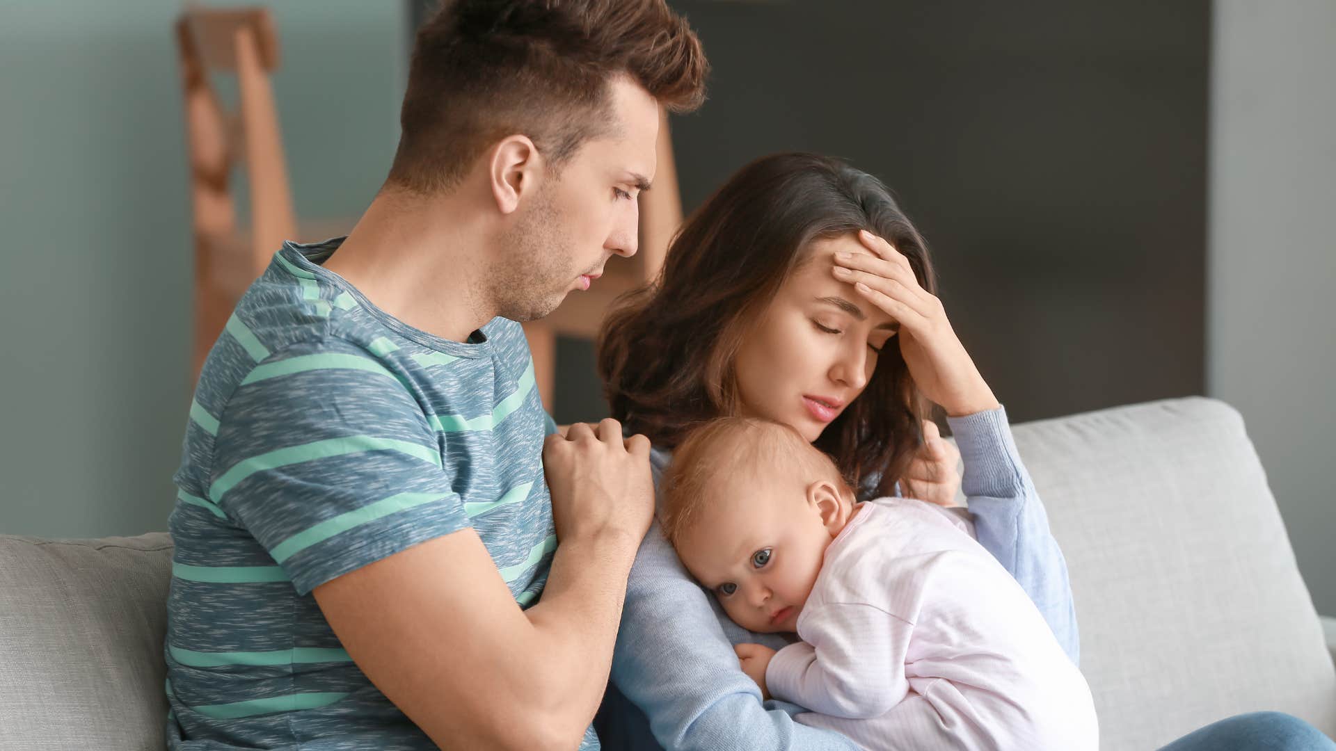 stressed mother holding baby while husband tries to comfort her