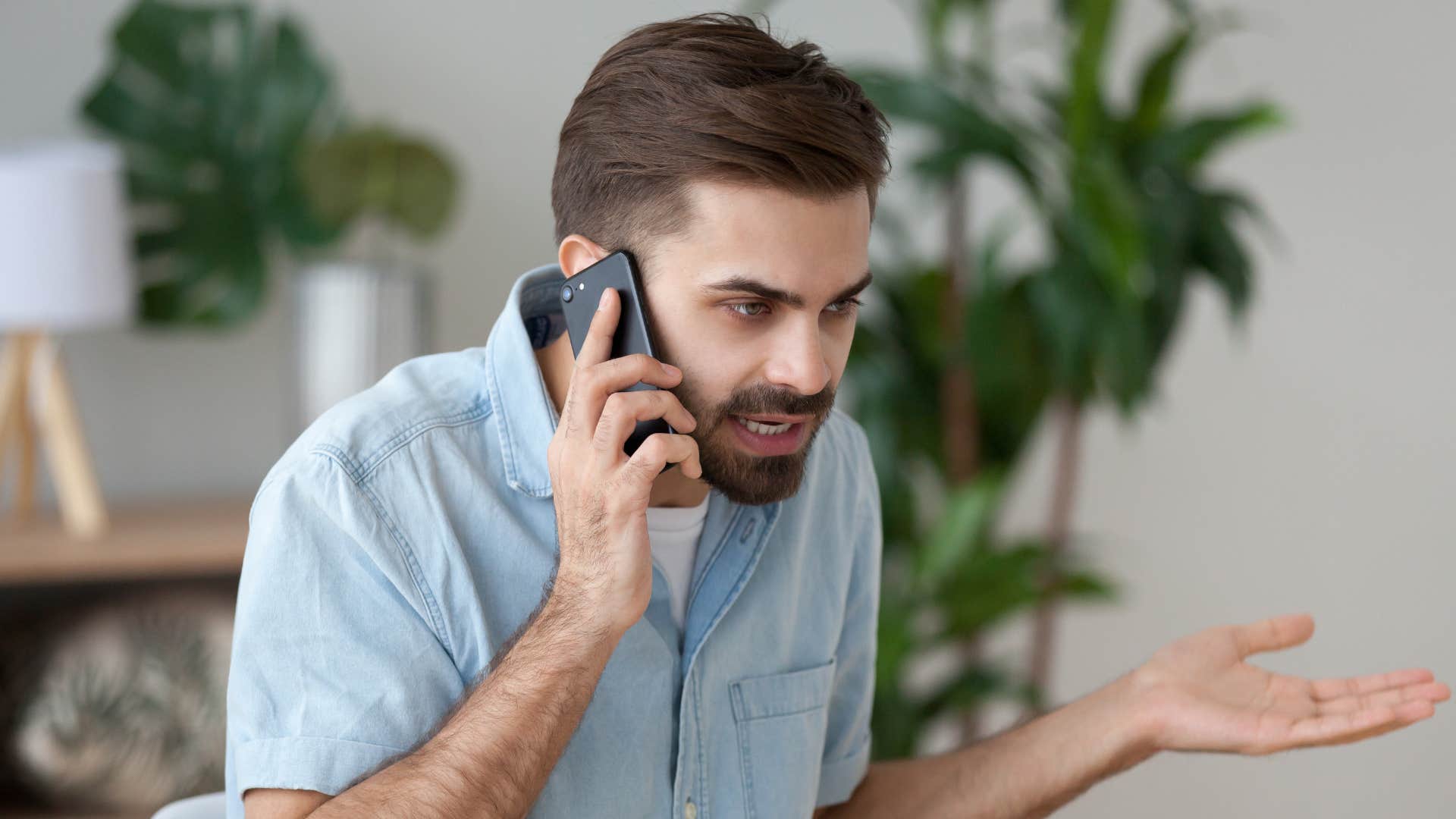 man in blue shirt growing angry as person on the phone responds without listening 