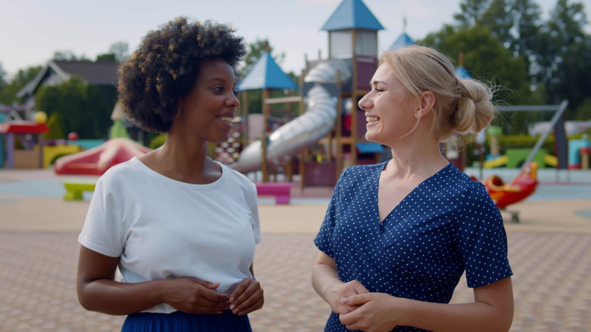 a mother compliments another mom at the playground as their children play