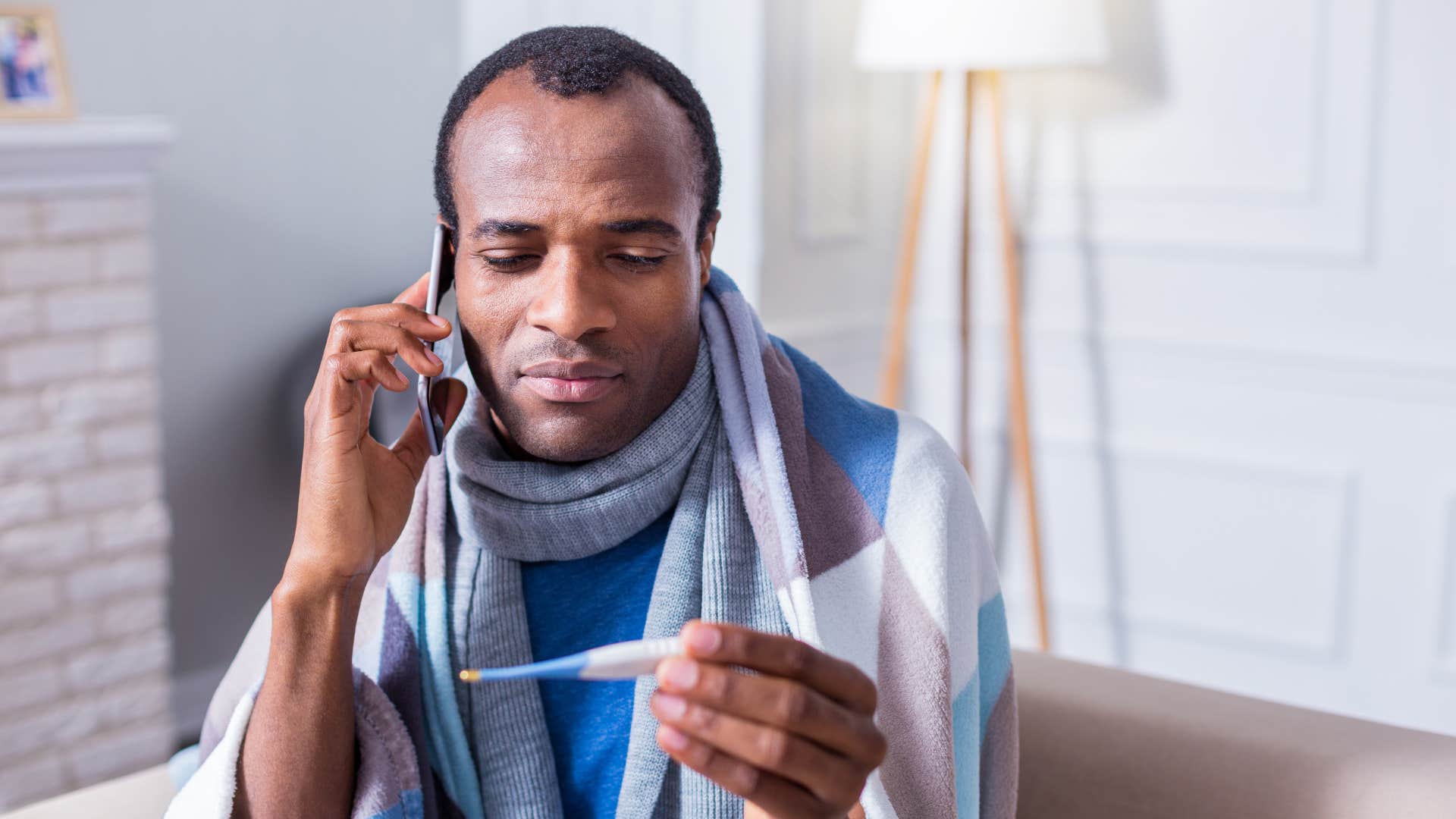 man on the phone saying he's not feeling well holding thermometer