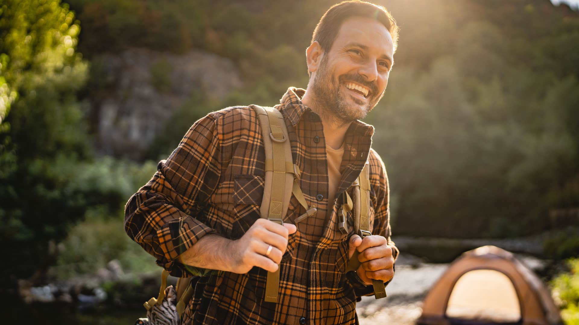 man in brown shirt going on a camping trip as he hokes and smiles
