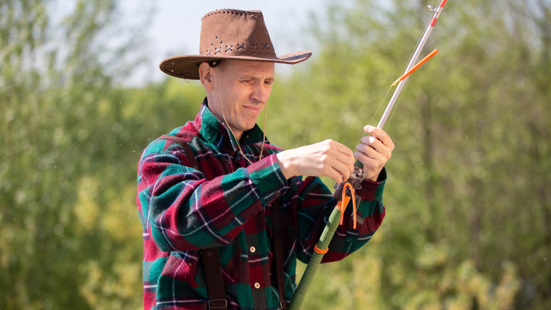 man in brown hat fishing as he holds pole
