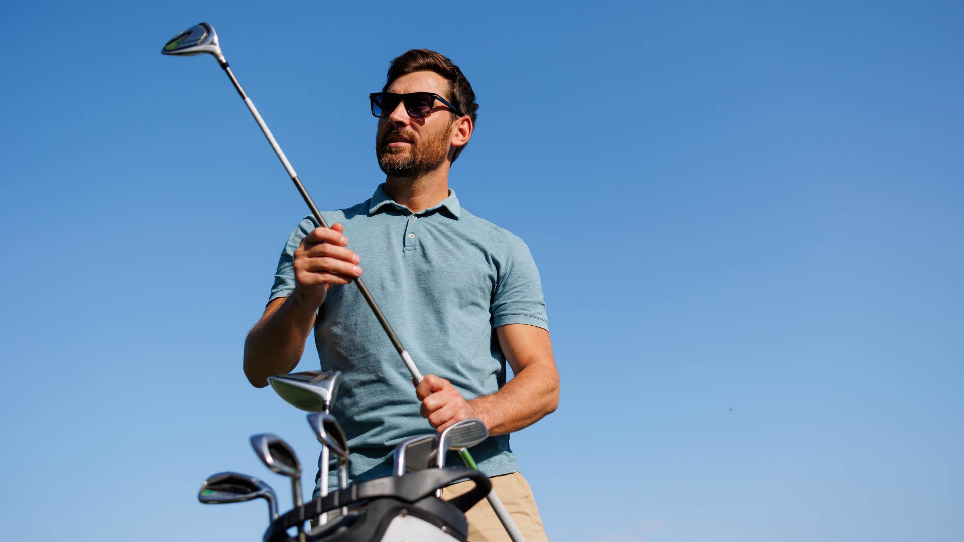 man golfing in blue shirt as he wears sunglasses 