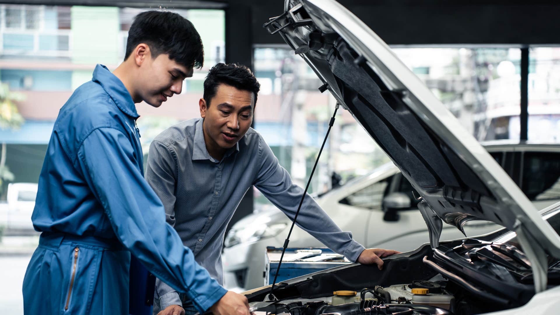 man in blue jumper and man in gray shirt looking at car engine as they do their best to restore car