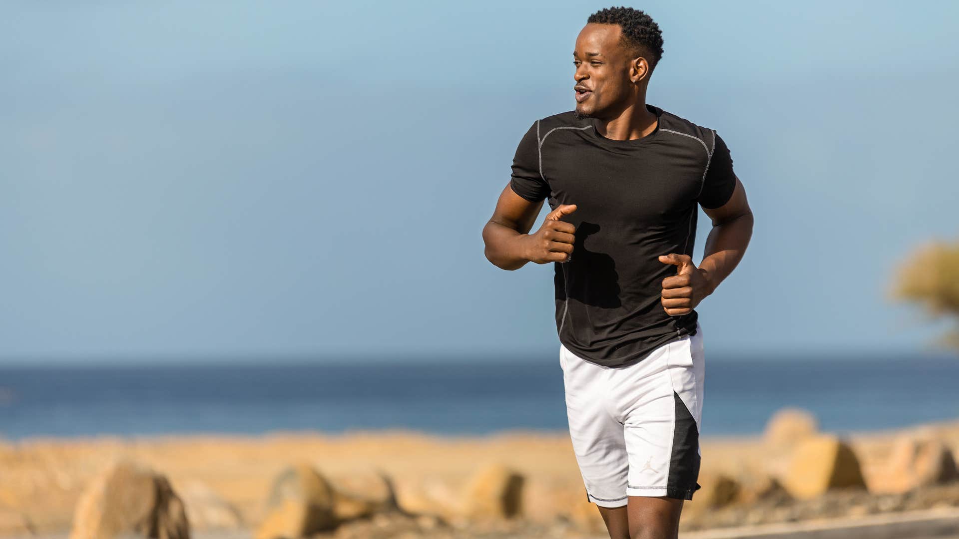 man in black shirt and white shorts running in a marathon near the beach