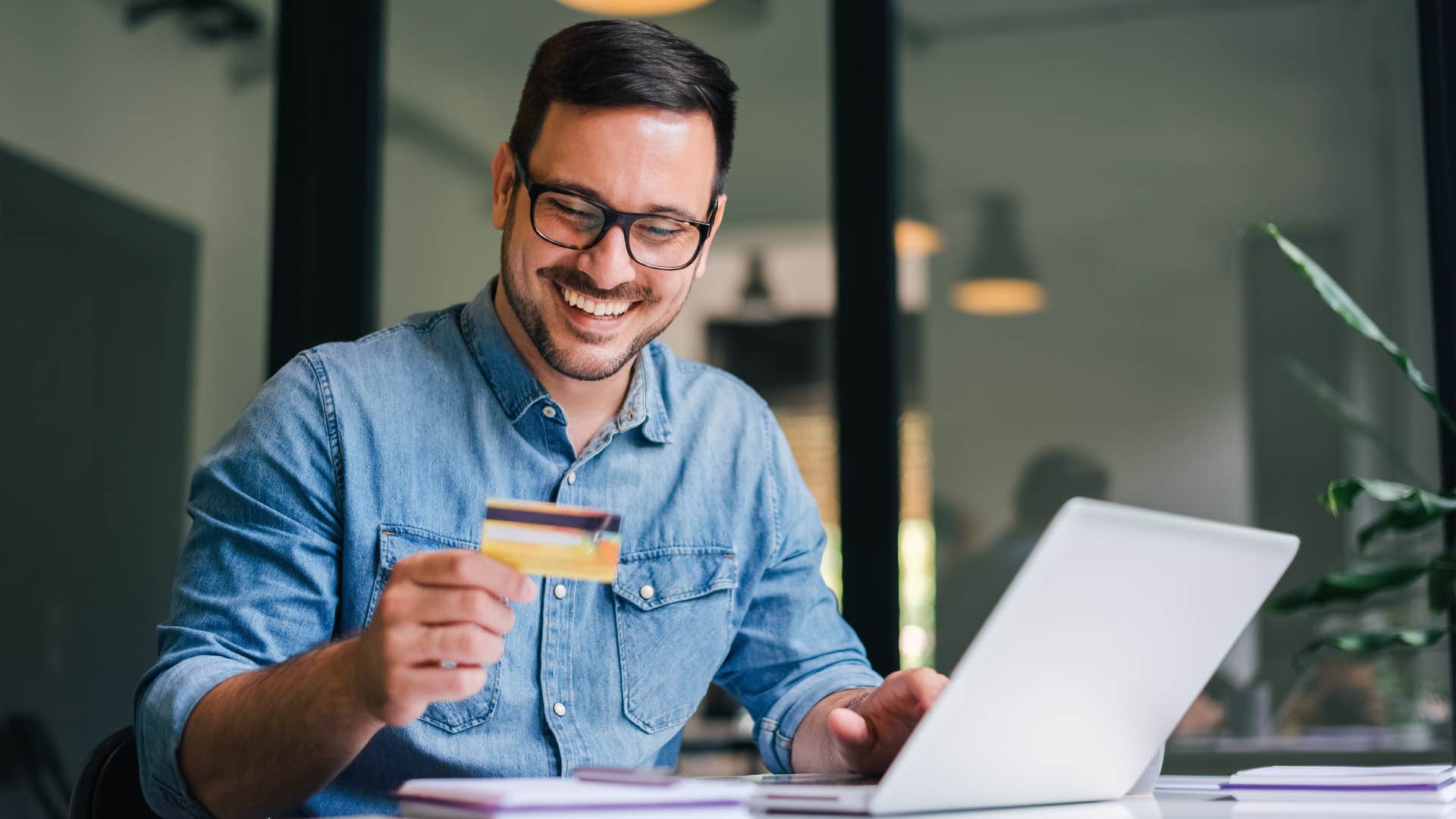 man in blue shirt being a collector as he pulls out card and buys another thing on his laptop