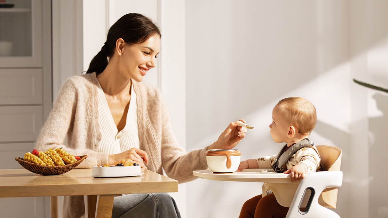 The One Essential Momcozy Item That Makes The Lives Of Toddler Parents So Much Easier mom feeding baby in momcozy dinerpal high chair