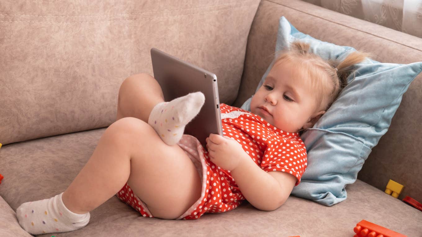 Pediatrician Reveals How Much Screen Time Is Safe For Children Under 2 Little girl under 2 using a screen while lying on the couch