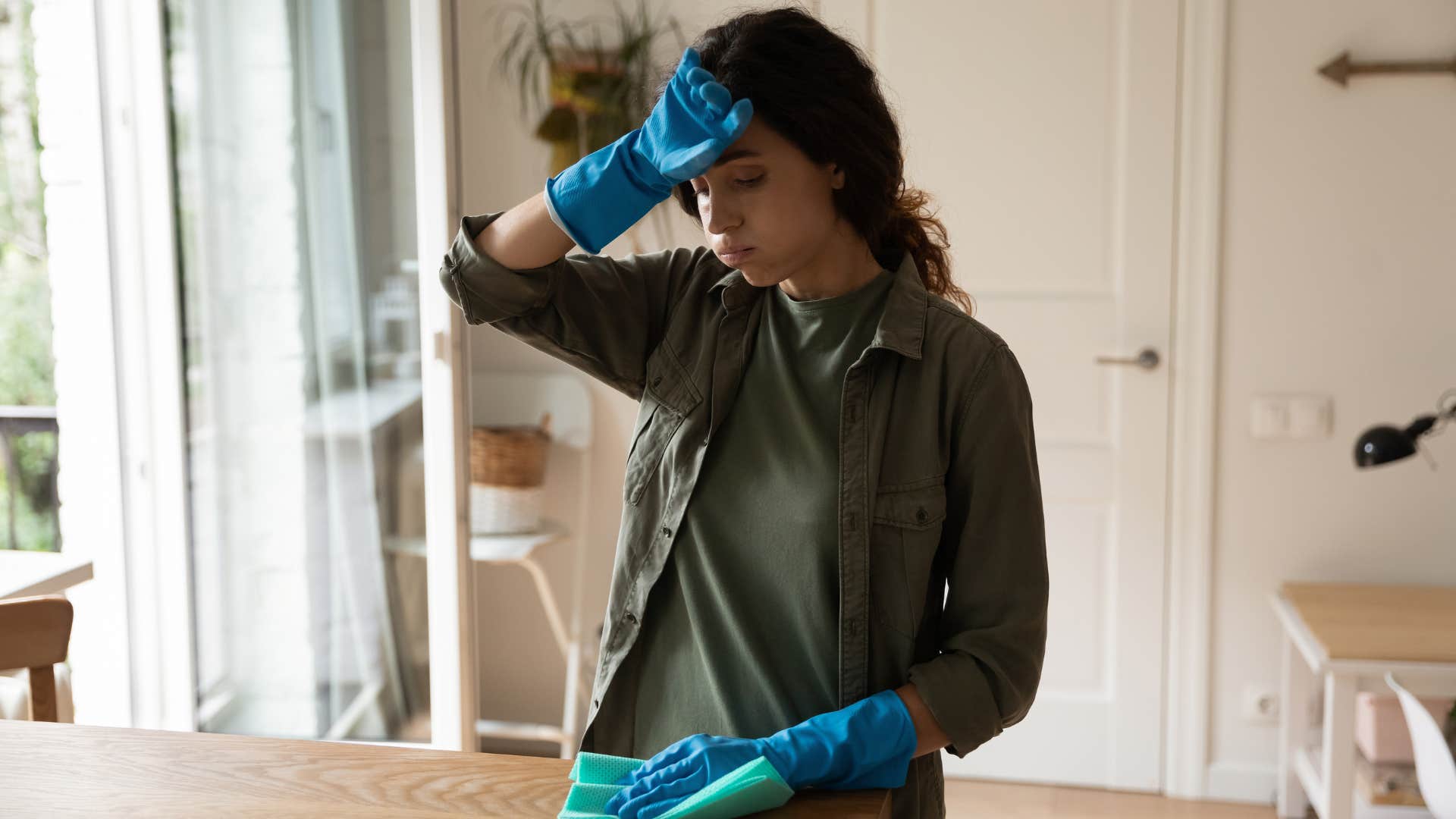 highly perfectionist woman in green shirt cleaning and putting hand on forehead 