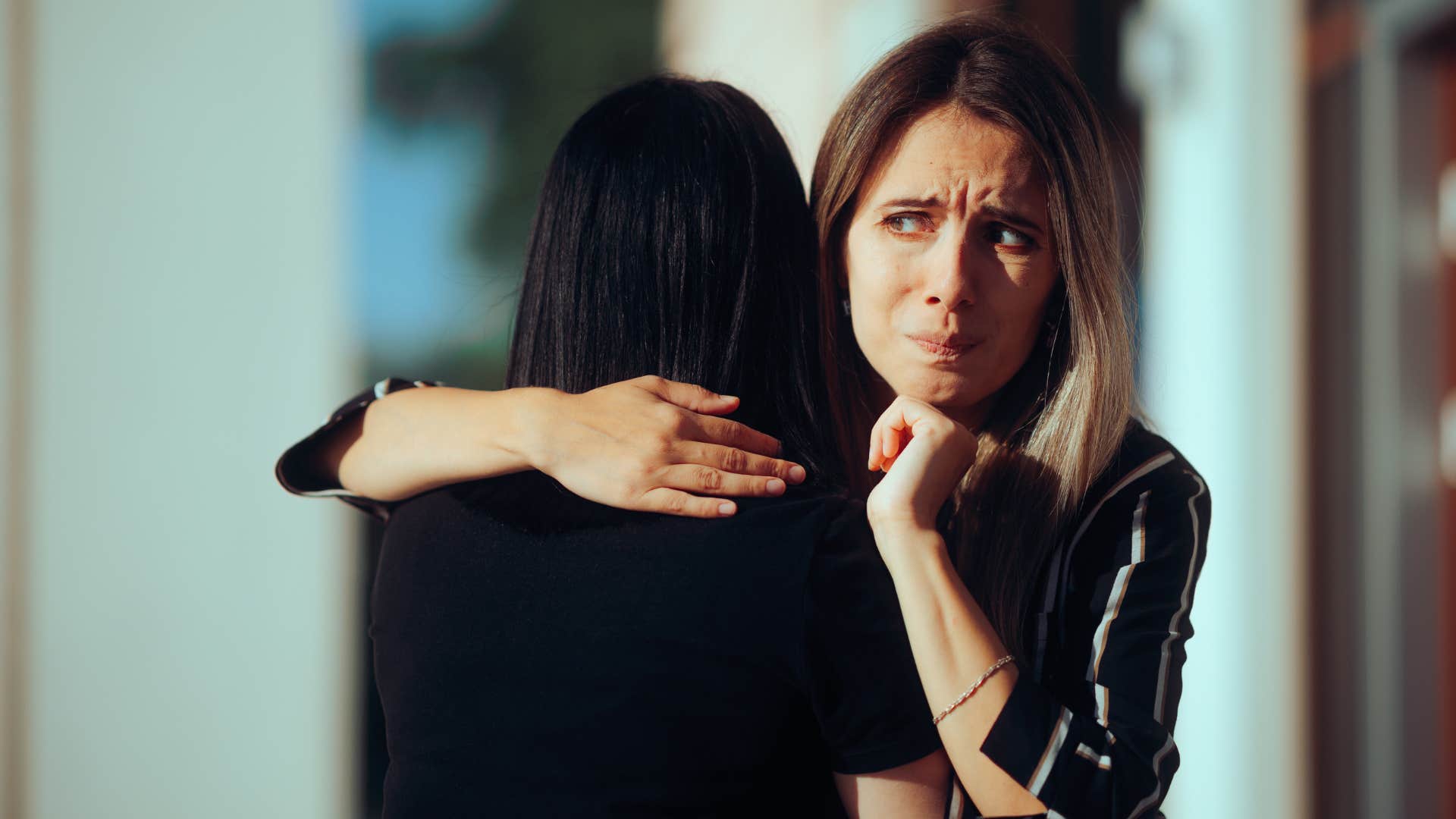 woman in black shirt lacking boundary as she tightly hugs friend who looks uncomfortable 