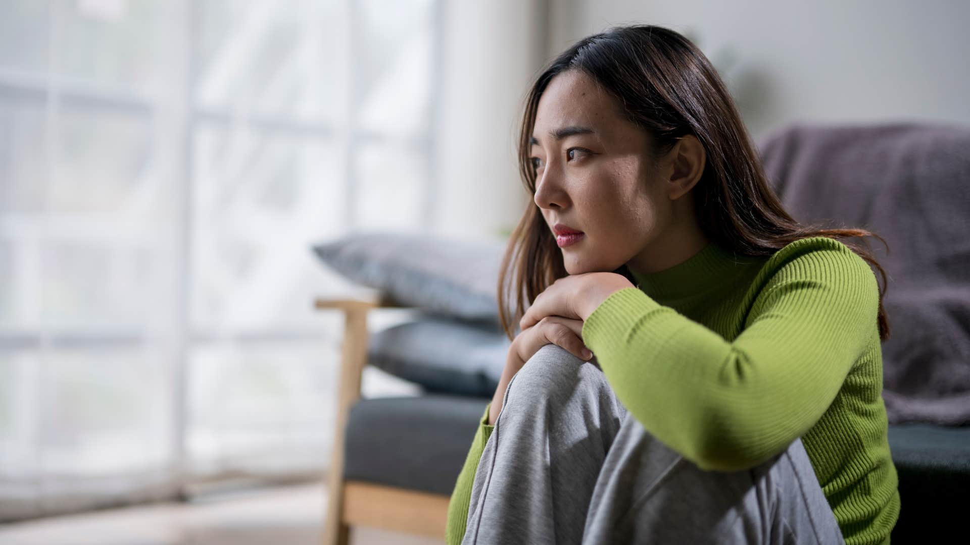 woman in green shirt has low self-esteem as she sits down on the floor and looks sad