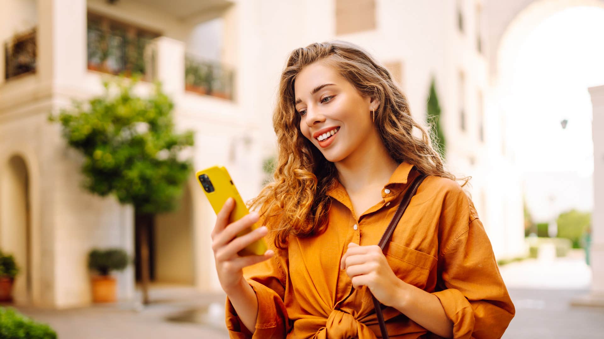 woman in orange shirt smiling and looking at phone as she likes messages or adding an emoji reaction while in a group chat