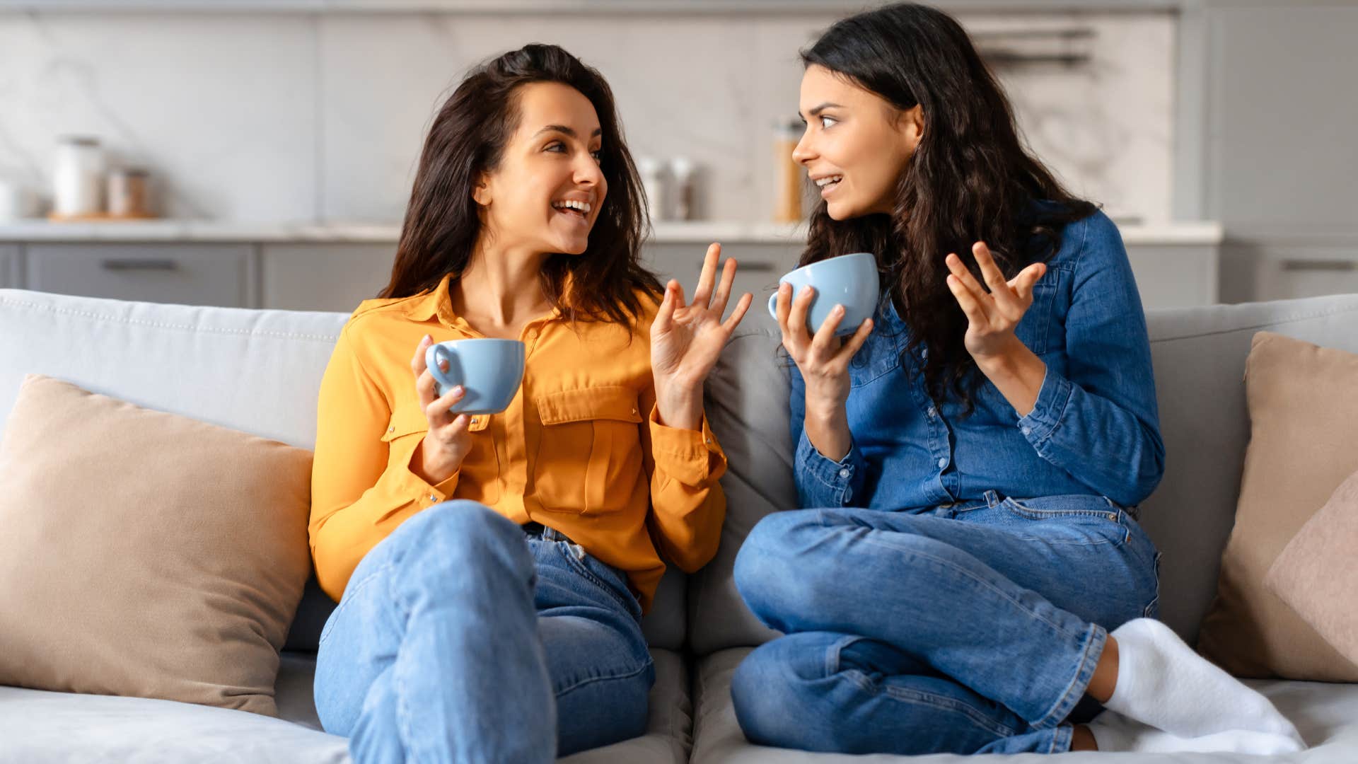 woman in blue shirt saying I have tea, and then refusing to spill it immediately as friend in orange shirt talks to her and drinks coffee together