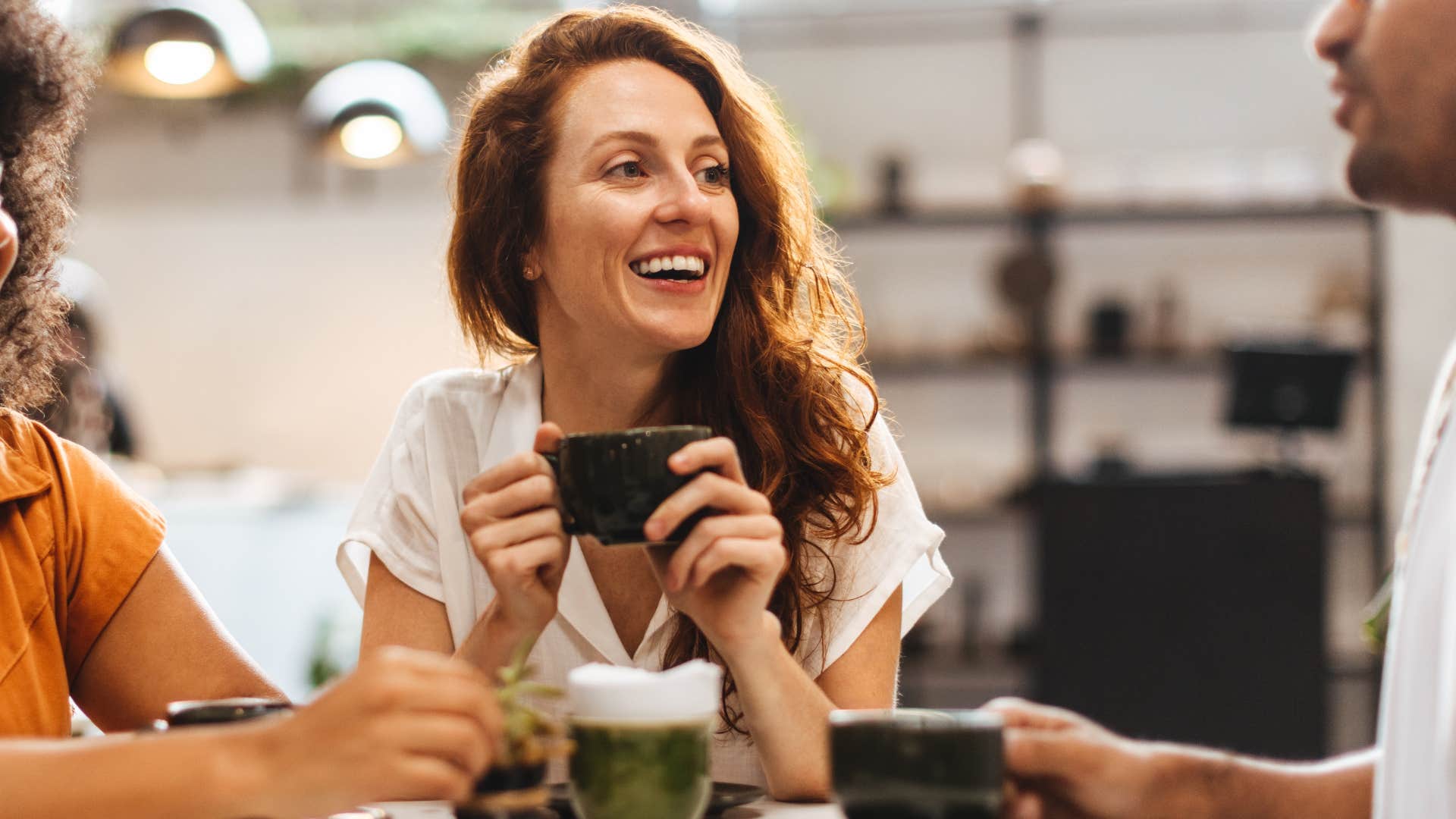 Emotionally intelligent woman smiling and drinking coffee with friends.