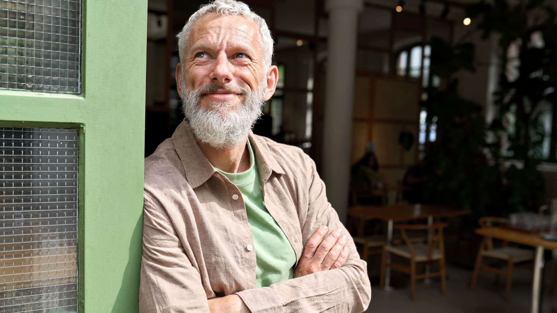 Sensitive man smiling and leaning against a door in a restaurant.